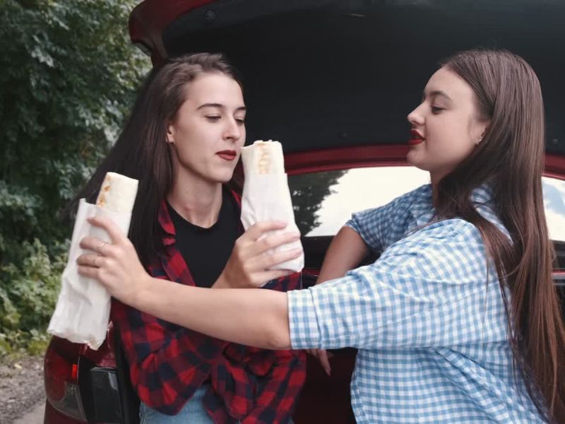 Dve devojčice u pubertetu sede ispred auta i jedu tortilje