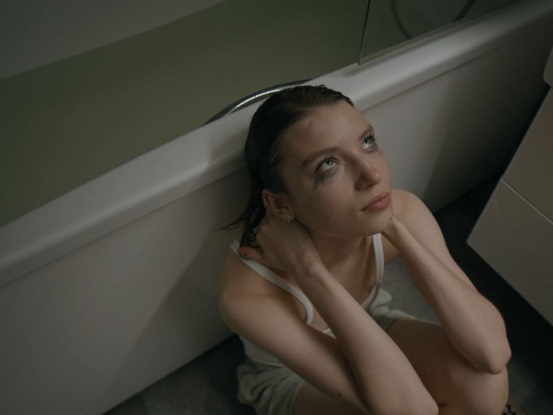 Devojka koja pati od anksioznosti sedi sa razmazanom maskarom naslonjena na kadu i drži se za vrat