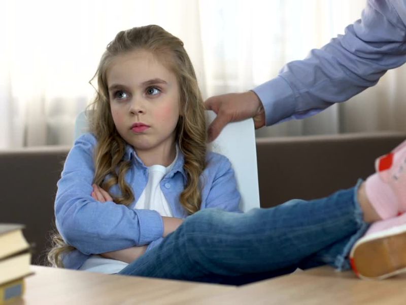 Devojčica sedi  ljuta sa prekrštenim rukama i  podignutim nogama na stolu