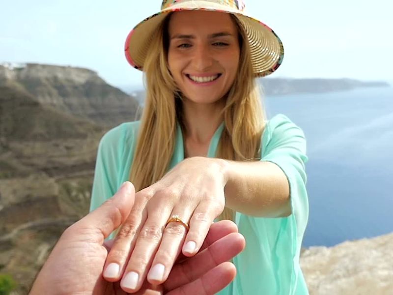 Zaprošena devojka stoji nasmejana na vrhu neke planine i pokazuje svoj verenički prsten