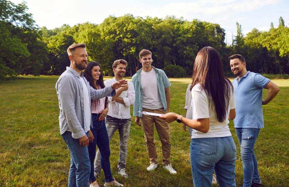 Grupa ljudi razgovara i učestvuje u team building aktivnosti na livadi u prirodi.